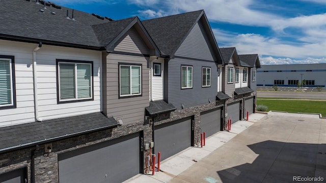 9250 Garnett Way Unit D, Arvada, CO 80007 - view of property exterior featuring stone siding, a garage, and a shingled roof