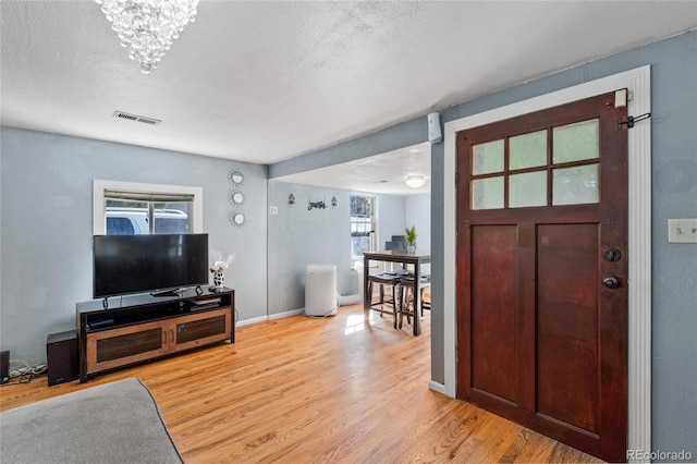 foyer with a textured ceiling, light hardwood / wood-style floors, and a notable chandelier