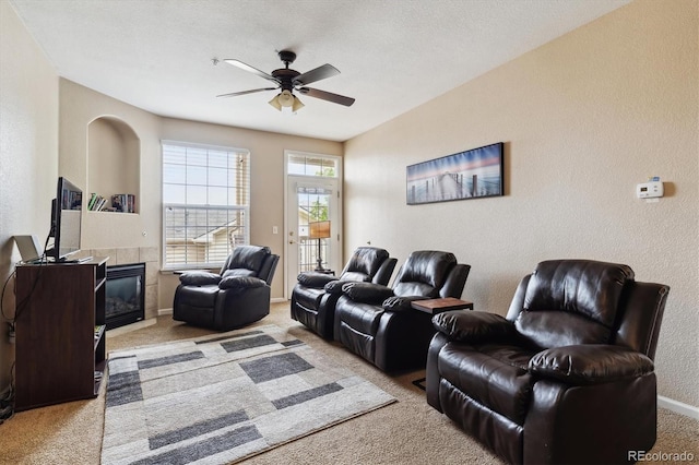 carpeted living room featuring ceiling fan, a textured ceiling, and a tiled fireplace