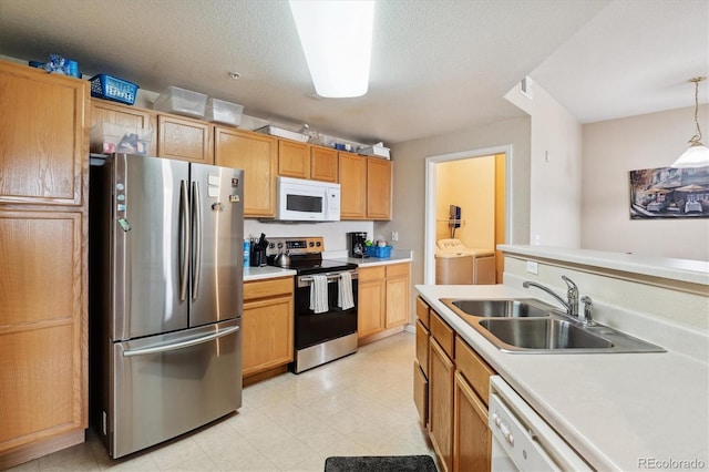 kitchen with appliances with stainless steel finishes, a textured ceiling, washing machine and clothes dryer, hanging light fixtures, and sink