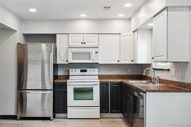 kitchen featuring light hardwood / wood-style floors, appliances with stainless steel finishes, white cabinetry, sink, and dark stone countertops