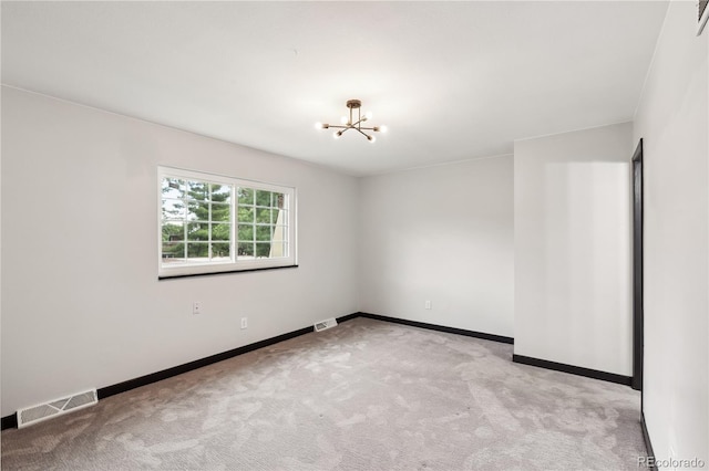 empty room featuring light colored carpet and a notable chandelier