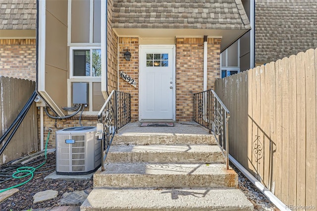 6492 Simms St Unit A, Arvada, CO 80004 - property entrance featuring central AC, brick siding, roof with shingles, and fence