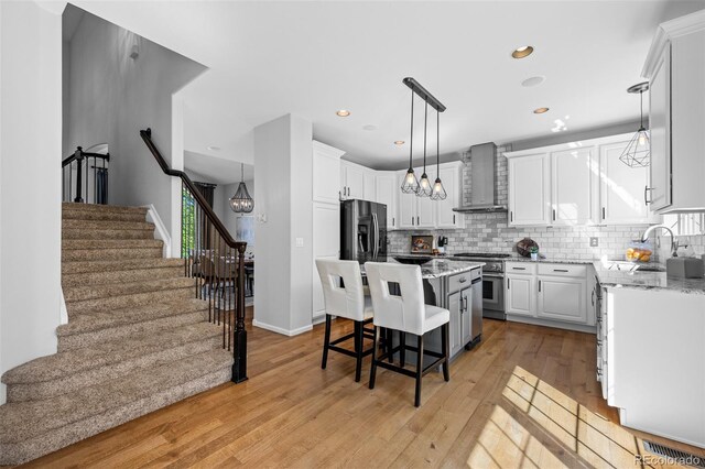 2880 Breezy Ln, Castle Rock, CO 80109 - kitchen with wall chimney range hood, appliances with stainless steel finishes, a kitchen island, a breakfast bar, and light wood finished floors