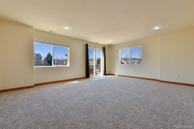 carpeted spare room featuring a wealth of natural light, visible vents, and baseboards