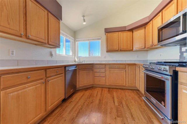 kitchen featuring light wood finished floors, tile counters, vaulted ceiling, stainless steel appliances, and a sink