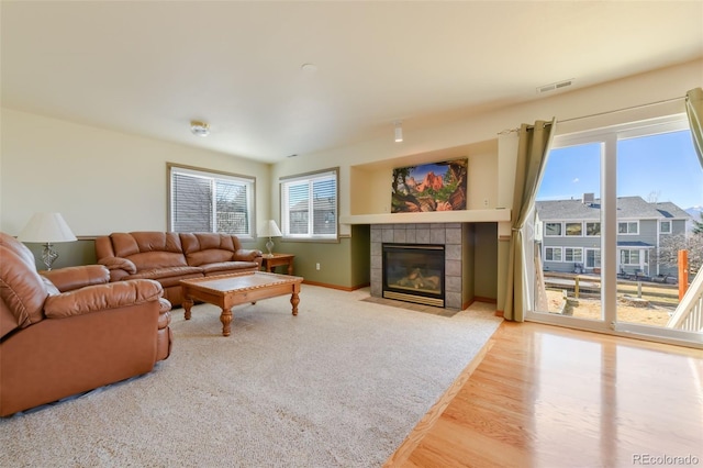 living room featuring wood finished floors, a fireplace, baseboards, and visible vents