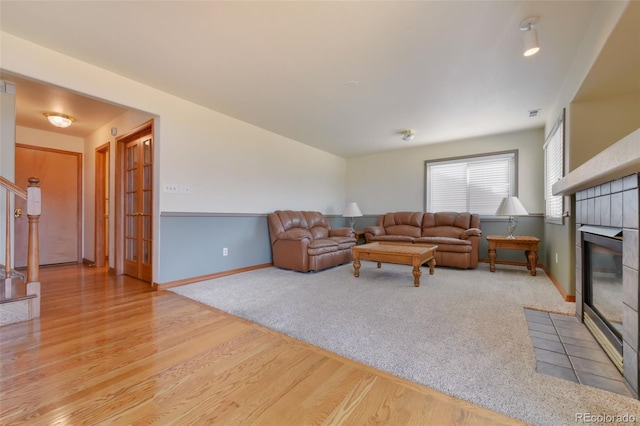 living room with stairway, wood finished floors, baseboards, a tile fireplace, and carpet flooring