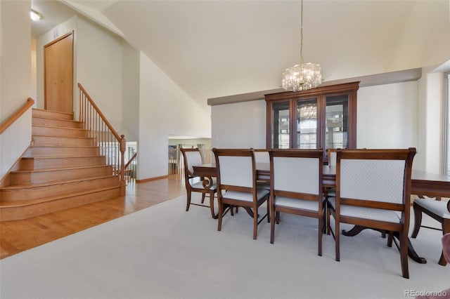 dining room with an inviting chandelier, stairway, wood finished floors, and high vaulted ceiling