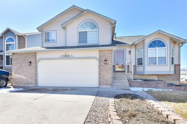 tri-level home with a garage, brick siding, and concrete driveway