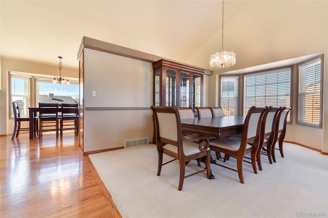 dining space with light wood finished floors, visible vents, baseboards, a notable chandelier, and high vaulted ceiling