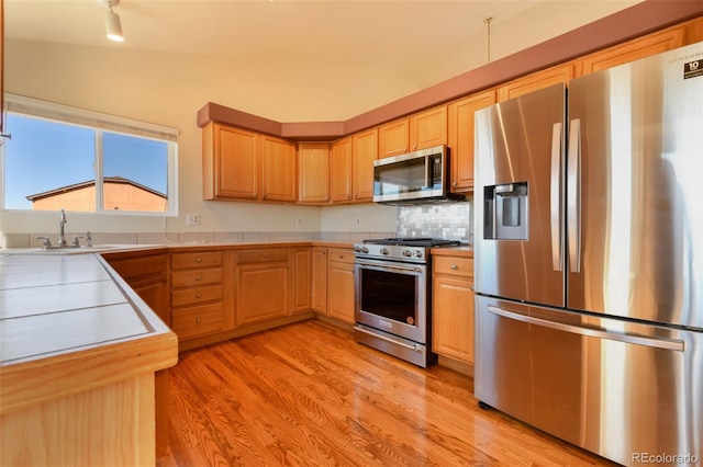 kitchen featuring light wood finished floors, light brown cabinets, light countertops, stainless steel appliances, and a sink