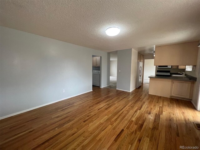 kitchen with light brown cabinetry, light wood-type flooring, refrigerator, a textured ceiling, and sink