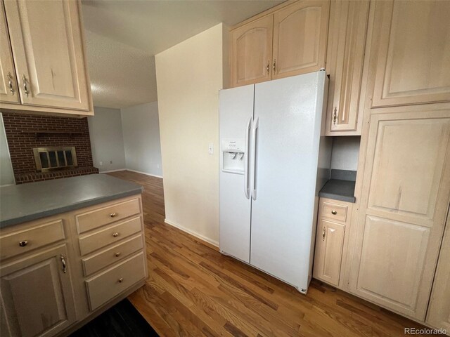 kitchen with hardwood / wood-style floors, white refrigerator with ice dispenser, a textured ceiling, and a brick fireplace