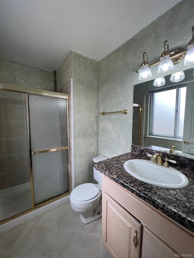 bathroom featuring tile patterned flooring, vanity, toilet, and a shower with door