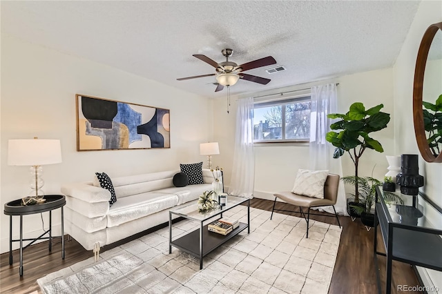 living room with ceiling fan, a textured ceiling, and light wood-type flooring