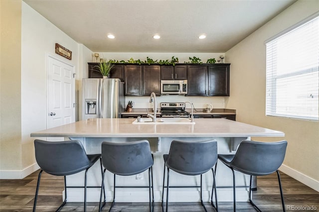13644 Ulster St, Thornton, CO 80602 - kitchen with stainless steel appliances, an island with sink, baseboards, dark brown cabinetry, and a kitchen breakfast bar