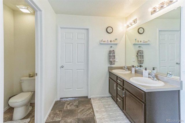 13644 Ulster St, Thornton, CO 80602 - bathroom featuring toilet, double vanity, baseboards, and stone finish floors
