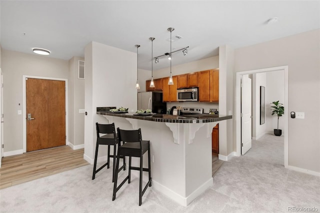 kitchen featuring a breakfast bar, decorative light fixtures, light carpet, appliances with stainless steel finishes, and kitchen peninsula