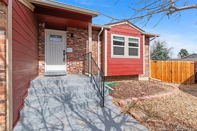 view of exterior entry with brick siding and fence