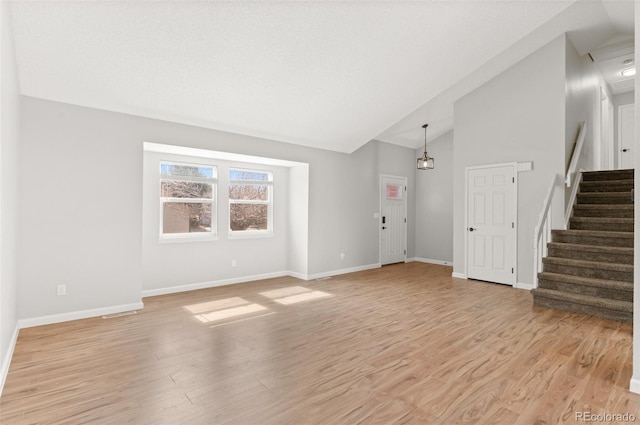 unfurnished living room with light wood-style flooring, high vaulted ceiling, stairs, and baseboards