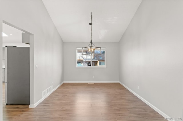 unfurnished dining area featuring an inviting chandelier, wood finished floors, visible vents, and baseboards