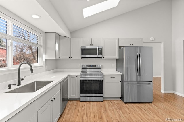 kitchen featuring lofted ceiling with skylight, light wood-style flooring, a sink, stainless steel appliances, and light countertops