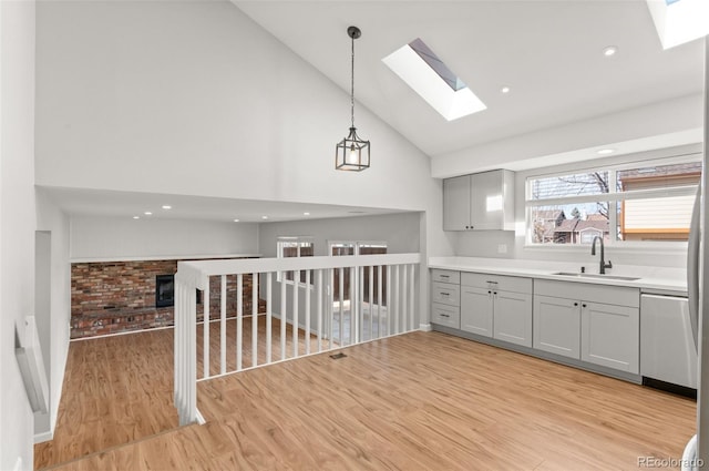 kitchen with gray cabinetry, dishwasher, light wood-type flooring, a skylight, and a sink