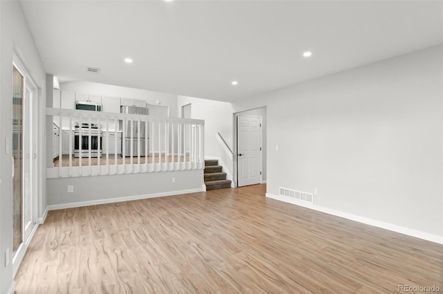 unfurnished living room featuring visible vents, recessed lighting, stairway, light wood finished floors, and baseboards