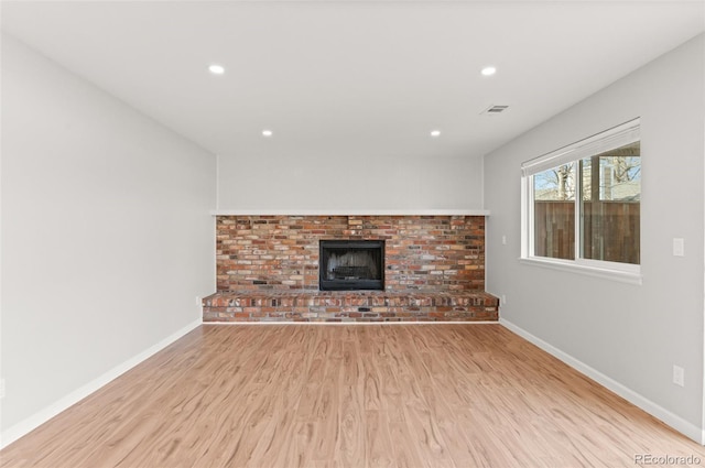 unfurnished living room featuring a brick fireplace, baseboards, and wood finished floors