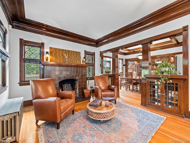 living area featuring ornate columns, ornamental molding, a tiled fireplace, and light hardwood / wood-style flooring