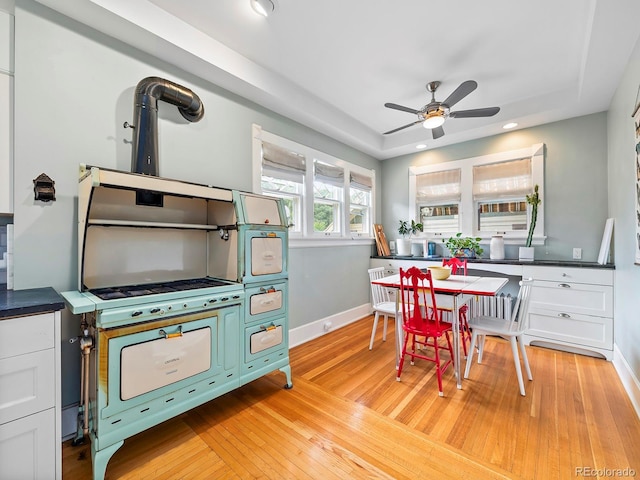 kitchen with a raised ceiling, ceiling fan, white cabinets, and light wood-type flooring