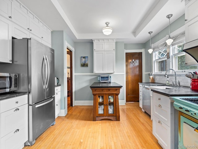 kitchen featuring a raised ceiling, appliances with stainless steel finishes, pendant lighting, and white cabinets