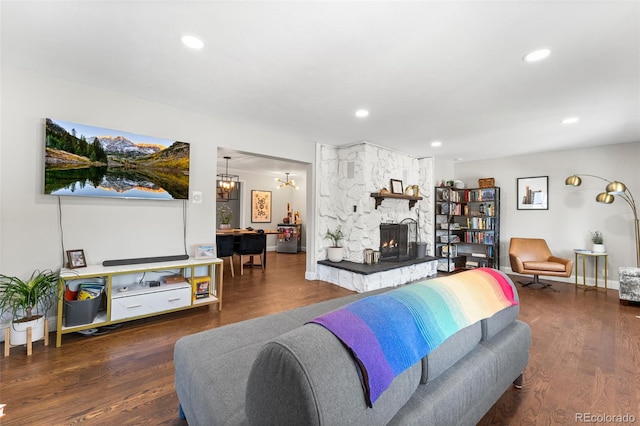 living room with a stone fireplace, a notable chandelier, and dark wood-type flooring