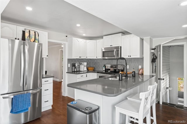 kitchen with kitchen peninsula, dark hardwood / wood-style floors, a kitchen bar, white cabinets, and appliances with stainless steel finishes