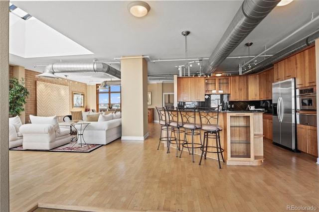 kitchen with decorative backsplash, appliances with stainless steel finishes, brick wall, and light hardwood / wood-style flooring