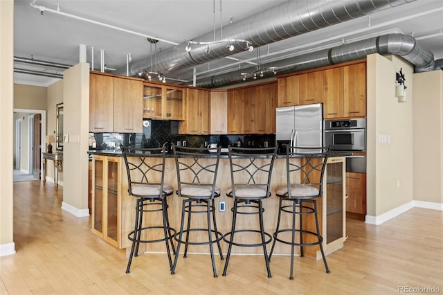 kitchen featuring light wood-type flooring, a kitchen breakfast bar, decorative backsplash, and stainless steel appliances