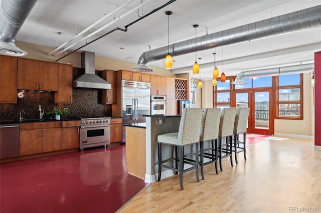 kitchen with a kitchen bar, hardwood / wood-style floors, hanging light fixtures, wall chimney exhaust hood, and high quality appliances