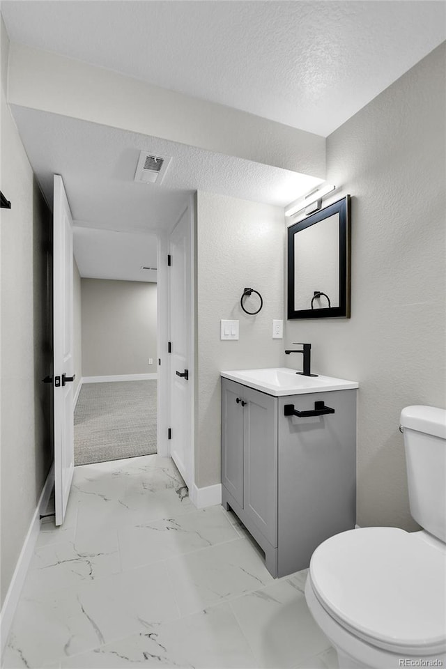10431 Holland St, Broomfield, CO 80021 - bathroom featuring vanity, baseboards, toilet, marble look tile flooring, and a textured ceiling