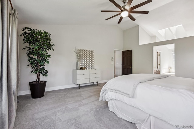 carpeted bedroom with ceiling fan, vaulted ceiling with skylight, and ensuite bathroom