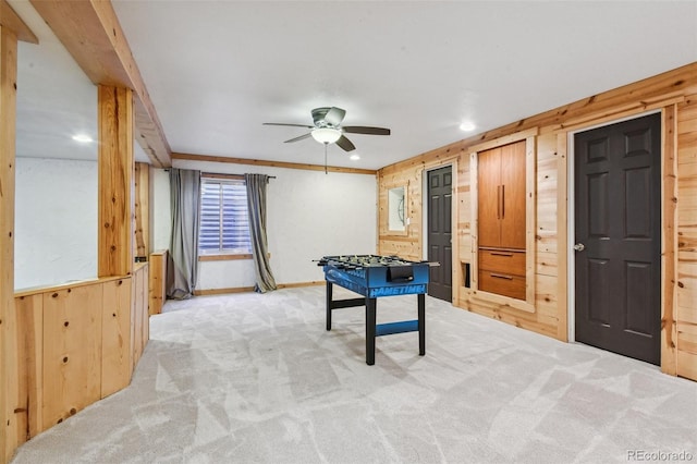 game room with wooden walls, ceiling fan, light colored carpet, and ornamental molding