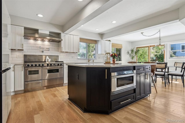 kitchen with white cabinets, wall chimney range hood, and appliances with stainless steel finishes