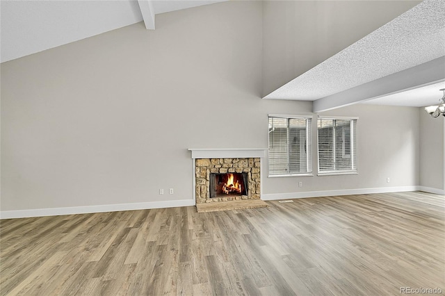 3890 S Atchison Way Unit B, Aurora, CO 80014 - unfurnished living room featuring wood finished floors, a chandelier, beam ceiling, a stone fireplace, and high vaulted ceiling