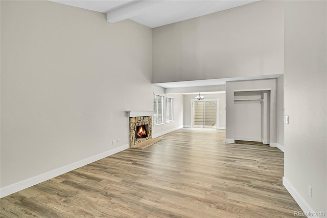 3890 S Atchison Way Unit B, Aurora, CO 80014 - unfurnished living room with high vaulted ceiling, beamed ceiling, wood finished floors, a chandelier, and a stone fireplace