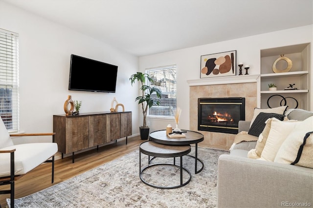 living area featuring built in shelves, baseboards, wood finished floors, and a tile fireplace