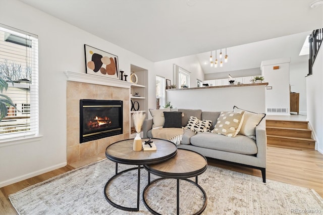 living room featuring visible vents, baseboards, vaulted ceiling, light wood finished floors, and a tiled fireplace