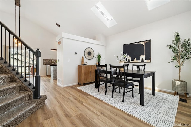 dining space with stairs, light wood-type flooring, a skylight, and baseboards