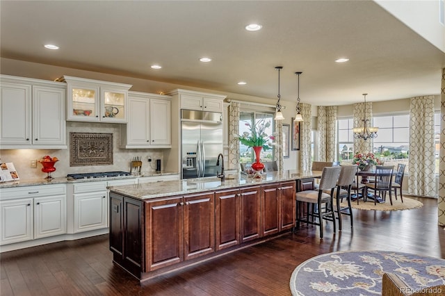 kitchen with backsplash, pendant lighting, a center island with sink, stainless steel appliances, and white cabinets