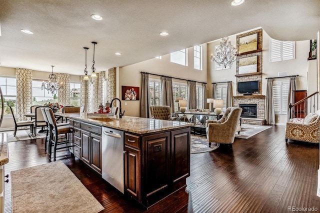 kitchen featuring a stone fireplace, a kitchen island with sink, dishwasher, dark brown cabinetry, and sink