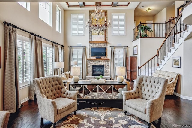 living room with dark wood-type flooring, a towering ceiling, a stone fireplace, and a chandelier